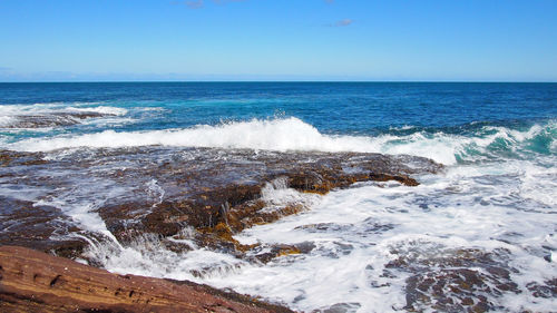 Waves splashing on shore against clear sky