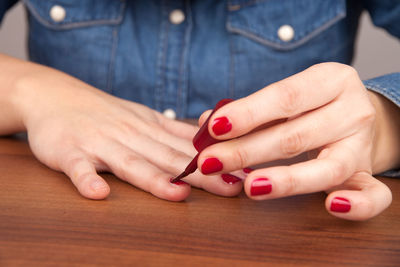 Midsection of woman painting fingernails at table
