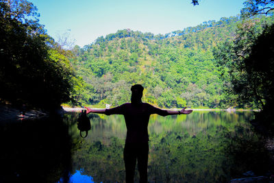 Rear view of man with arms outstretched standing by lake