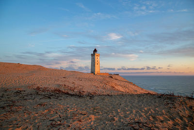 Lighthouse by sea against sky during sunset