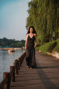 Full length portrait of woman standing on waterside against trees