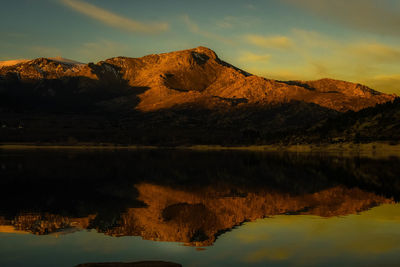 Scenic view of lake by mountain against sky during sunset