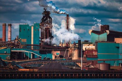 Smoke emitting from factories against cloudy sky