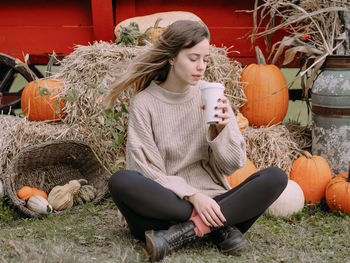 Full length of woman sitting by pumpkins