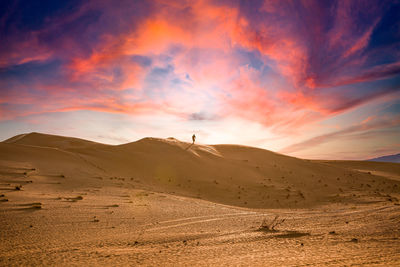 A man walking on sand dune 
view of desert against sky during sunset