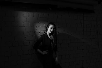 Woman with hand on hip standing against wall in darkroom