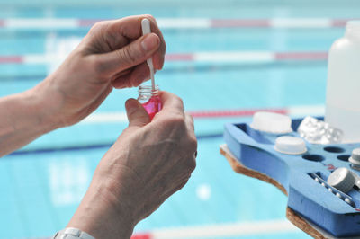 Cropped image of woman holding chemical against swimming pool