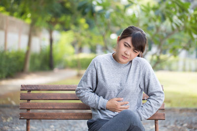 Young woman with stomachache sitting on park bench