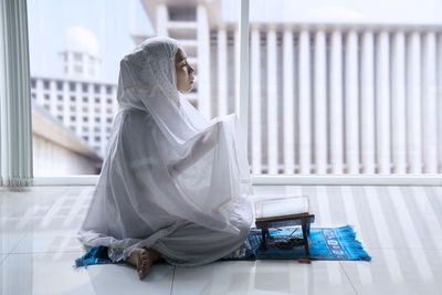 Side view of woman praying with koran on floor