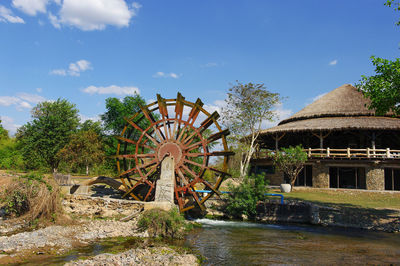 Gazebo and waterwheel by trees against sky at mekongfalls