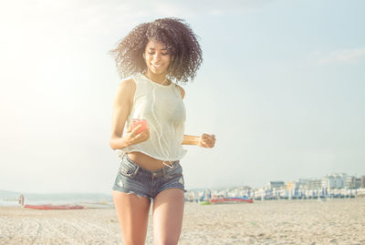 Portrait of smiling young woman standing on beach against sky