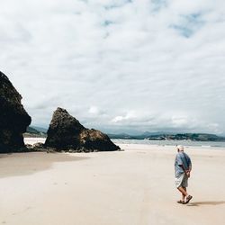 Rear view of man walking on beach against sky