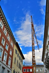 Low angle view of crane by building against sky