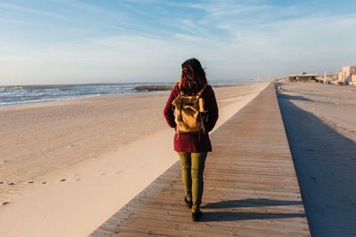 Rear view of woman standing on beach against sky