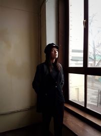 Young woman looking away while standing against window