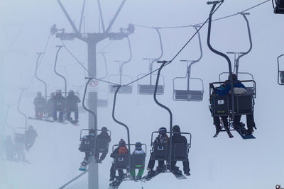 People travelling in ski lifts over snow covered field