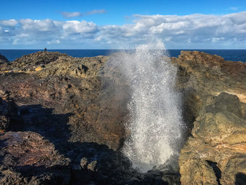 Waves splashing on rocks against sky