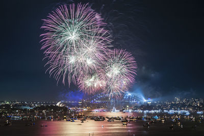 Firework display over illuminated city against sky at night