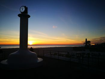 Silhouette railing by sea against sky during sunset