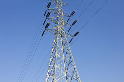 Low angle view of electricity pylon against clear blue sky