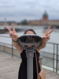 Woman looking through binoculars against railing and river