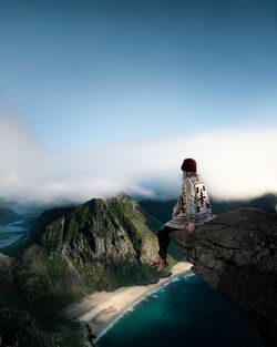 Girl sitting on rock looking at mountain against sky and beach