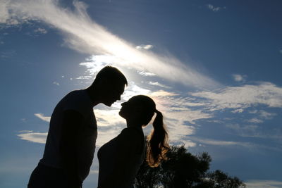 Low angle view of man and woman kissing against sky on sunny day