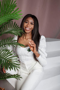 Glamour cropped fashion portrait of african woman with makeup sitting on stairs in white studio