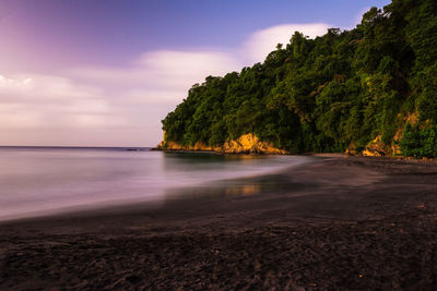 Scenic view of sea by rocky mountains against sky at dusk