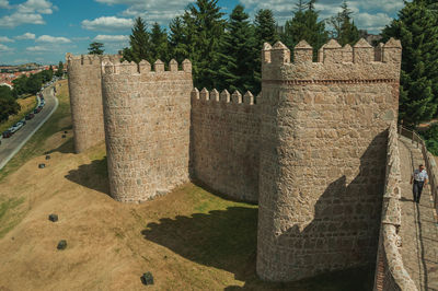  person on pathway over stone thick wall with large towers encircling the city of avila, in spain.