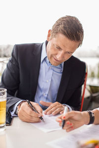 Businessman signing paperwork at outdoor cafe against clear sky