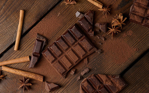 Broken pieces of dark chocolate, cinnamon sticks and star anise on a brown wooden table, top view