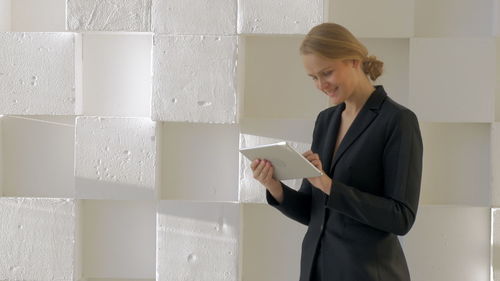 Woman holding mobile phone while standing against wall