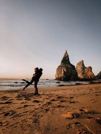 Man on rock at beach against clear sky