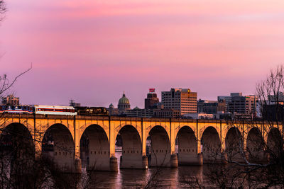 Arch bridge over river against sky during sunset