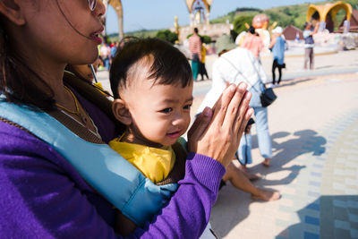 Midsection of woman praying while standing with son on footpath