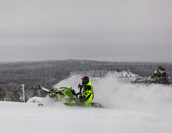 Man snowmobiling on field against cloudy sky