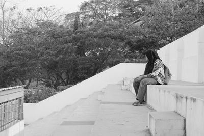 Woman sitting on retaining wall by staircase