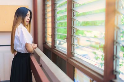 Side view of young woman standing against window