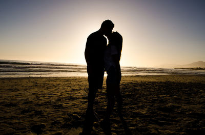 Silhouette man standing on beach against sky during sunset