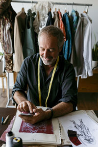 Smiling male tailor using smart phone at work studio