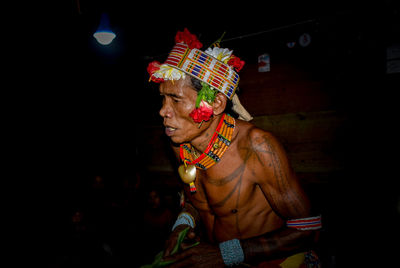 Shirtless man wearing headdress while standing in darkroom