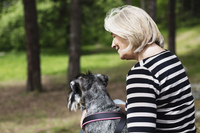 Side view of smiling senior woman sitting with dog at field