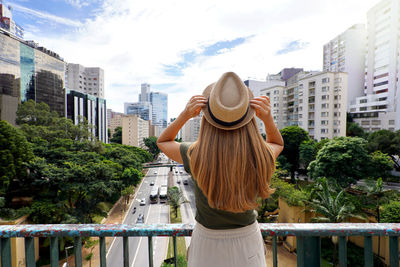 Back view of beautiful traveler girl holding hat enjoying view of sao paulo cityscape, brazil.