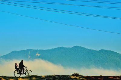 Man riding bicycle on mountain against blue sky