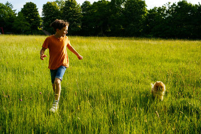 A boy runs through a summer field with small pomeranian dog