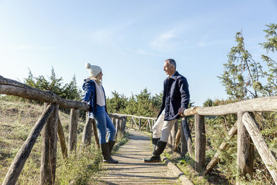 Man and woman looking at each other leaning on wooden bridge