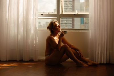 Young woman sitting on window at home