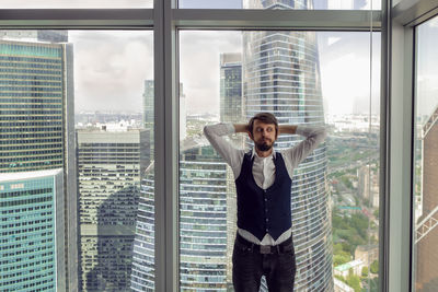 Thoughtful businessman with a beard stands ,next to the window in the office skyscrapers in moscow