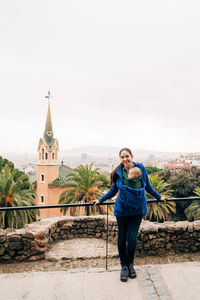 Full length of smiling young woman standing against building